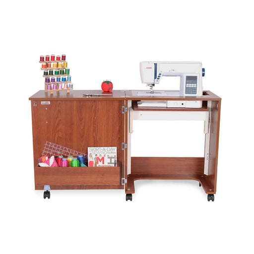 Arrow Judy 105 Sewing Cabinet in Teak with sewing machine installed, extended workspace, and front storage cubby filled with colorful thread and fabric.