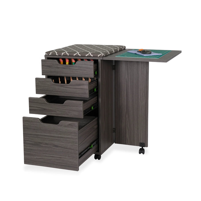 Kiwi Sewing Storage Cabinet by Arrow Sewing shown with open drawers displaying thread and tool organization, fold-out cutting table, and gray woodgrain finish on wheels.