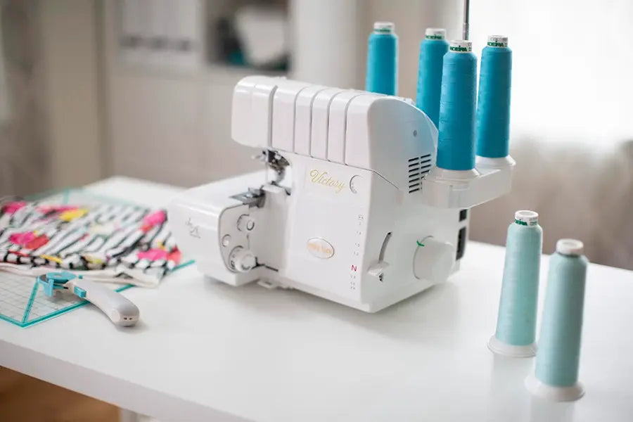 Baby Lock Victory Serger on sewing table with turquoise thread cones, professional serger for knits, hems, and fabric finishing.