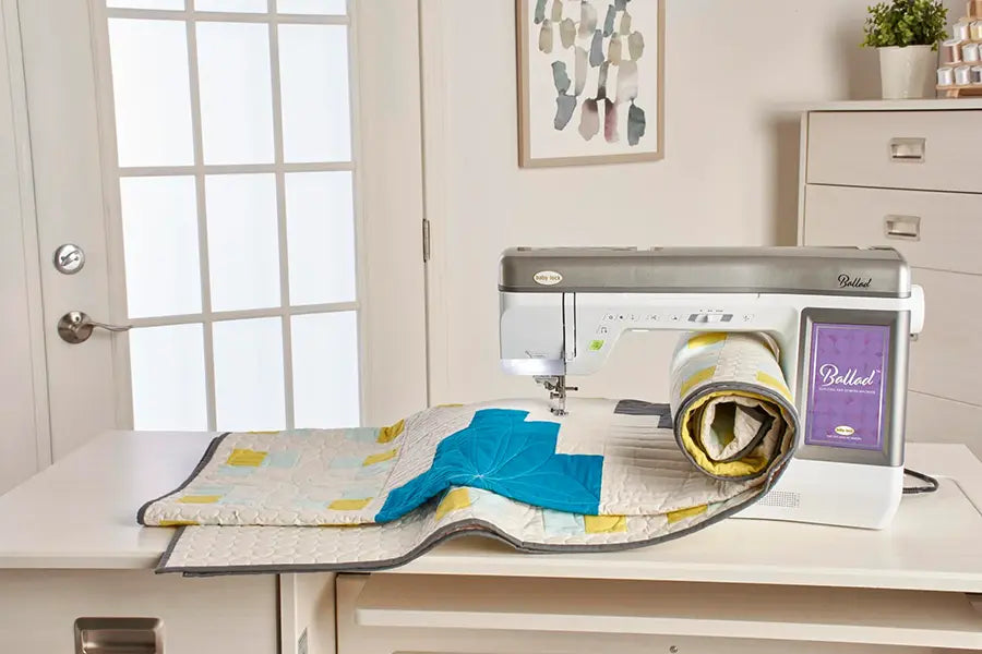 Baby Lock BLBA Ballad quilting and sewing machine shown with a completed quilt rolled across the workspace.