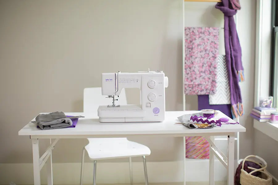 Baby Lock Zeal sewing machine in a home sewing room, displayed on a white table with crafting supplies nearby.