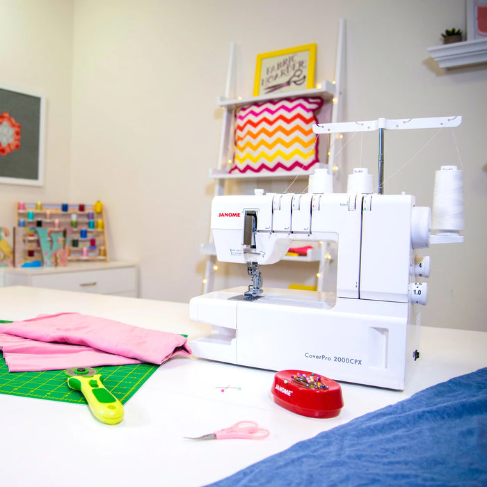 Janome CoverPro 2000CPX coverstitch machine set up in a sewing workspace with fabric and tools, demonstrating its use for garment construction and hemming.