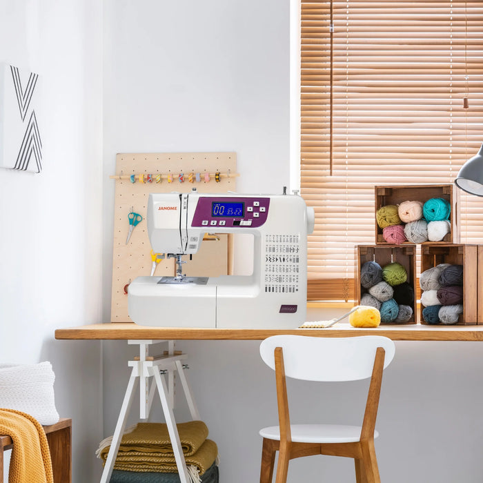 Janome 3160QDC-G sewing machine displayed in a modern craft room with yarn and sewing supplies.