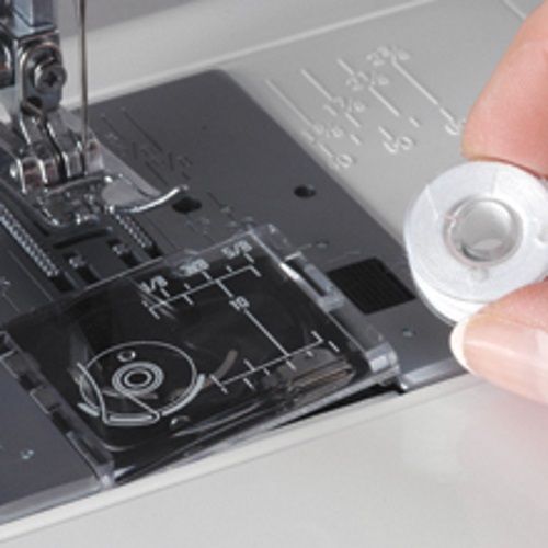 Janome 712T sewing machine drop-in bobbin system with user loading bobbin into transparent bobbin cover for easy threading.