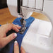 Hands guiding fabric through the Janome CoverPro 900CPX during a coverstitch hem, highlighting the machine’s wide workspace and stitch accuracy.