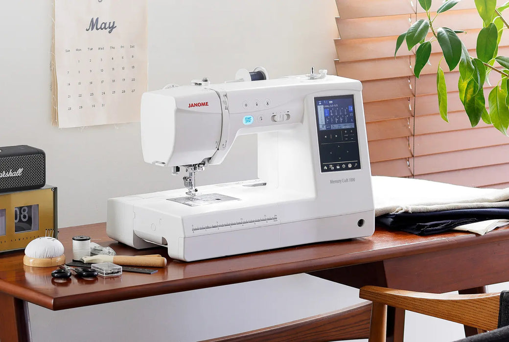 Janome Memory Craft 1000 sewing and embroidery machine displayed in a home sewing studio setup on a wooden table