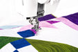 Janome Continental M6 performing free-motion quilting on colorful patchwork quilt with precision needle and foot.