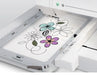 Janome MC550E Limited Edition embroidery machine stitching multicolor floral pattern in large hoop frame.
