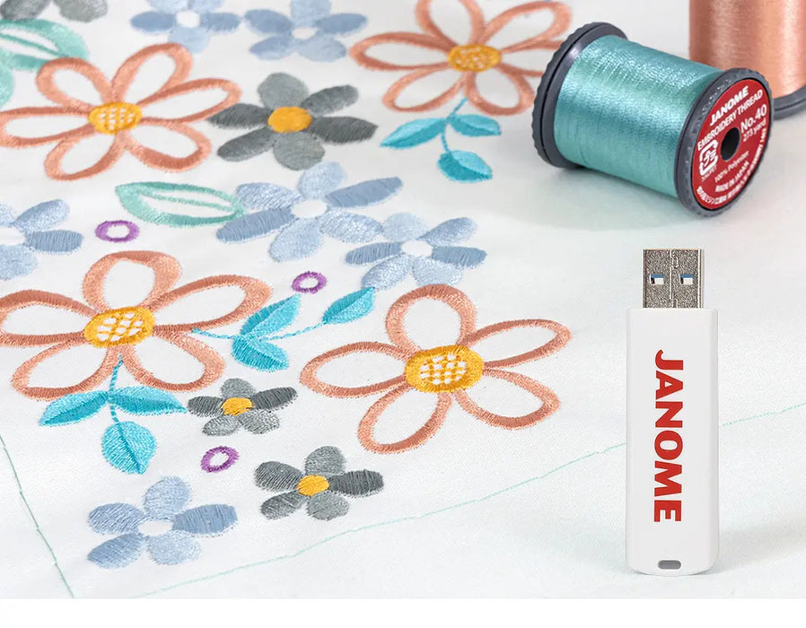 USB drive with exclusive Janome embroidery designs displayed next to finished multicolor floral embroidery sample