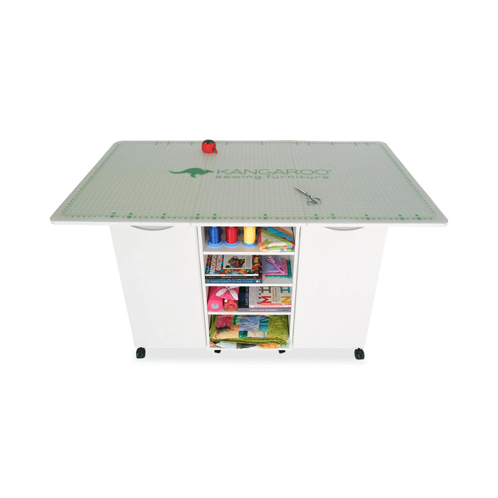 Top-down view of Ash White Kangaroo Kookaburra Cutting Table with cutting mat and organized rear storage shelves for sewing supplies.
