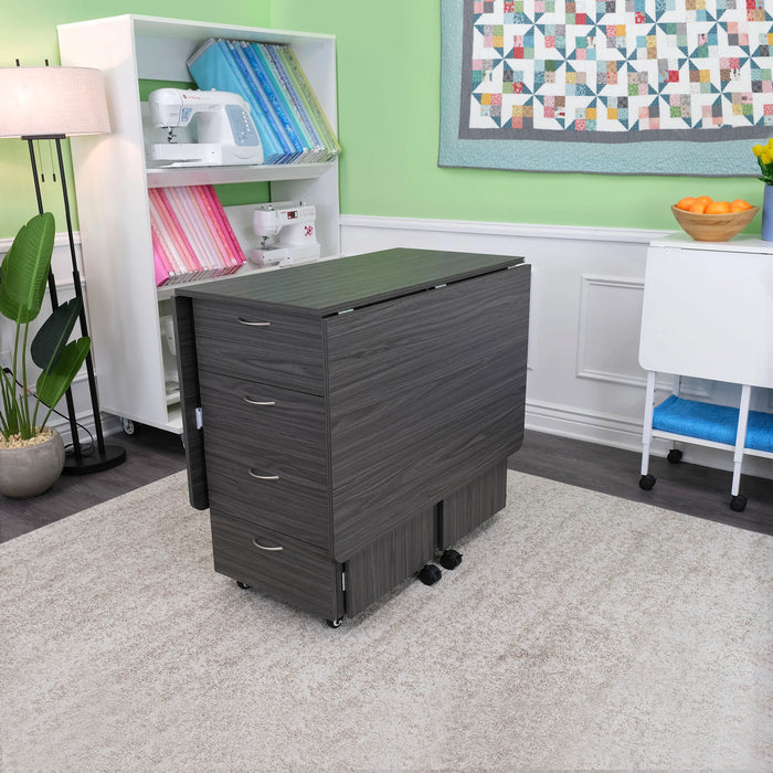 Gray Kangaroo Kookaburra Cutting Table folded for storage inside a sewing room, highlighting compact design and four front drawers.